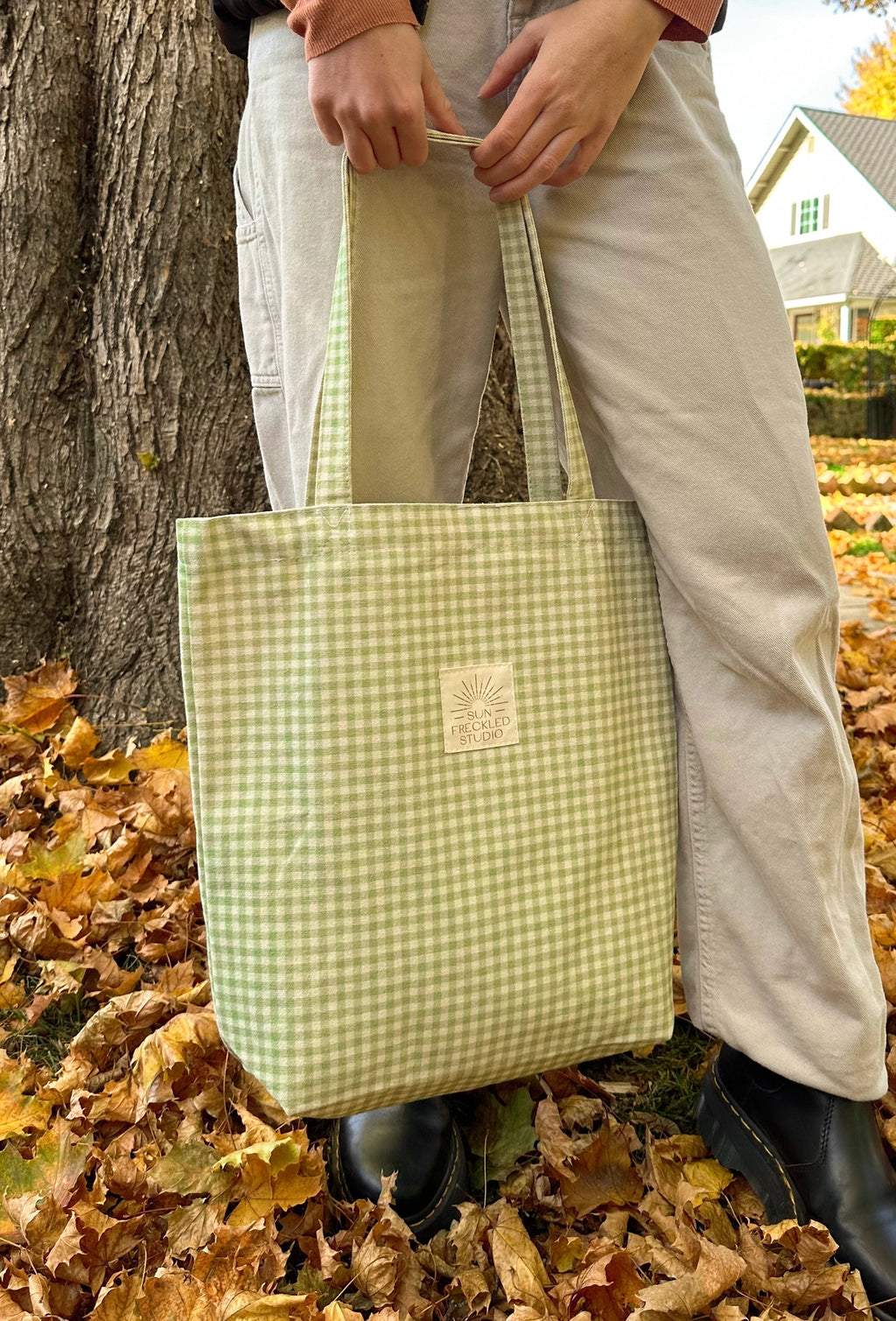 Person holding a sage green gingham canvas tote bag outdoors, everyday cotton tote with shoulder straps styled for casual errands.