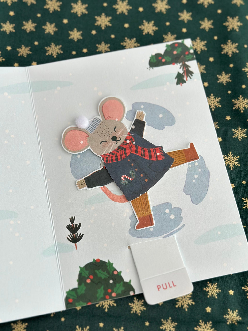 Close-up of animated mouse character after the tab is pulled, arms raised, candy cane in pocket, snowy background.