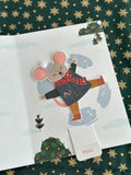 Close-up of animated mouse character after the tab is pulled, arms raised, candy cane in pocket, snowy background.