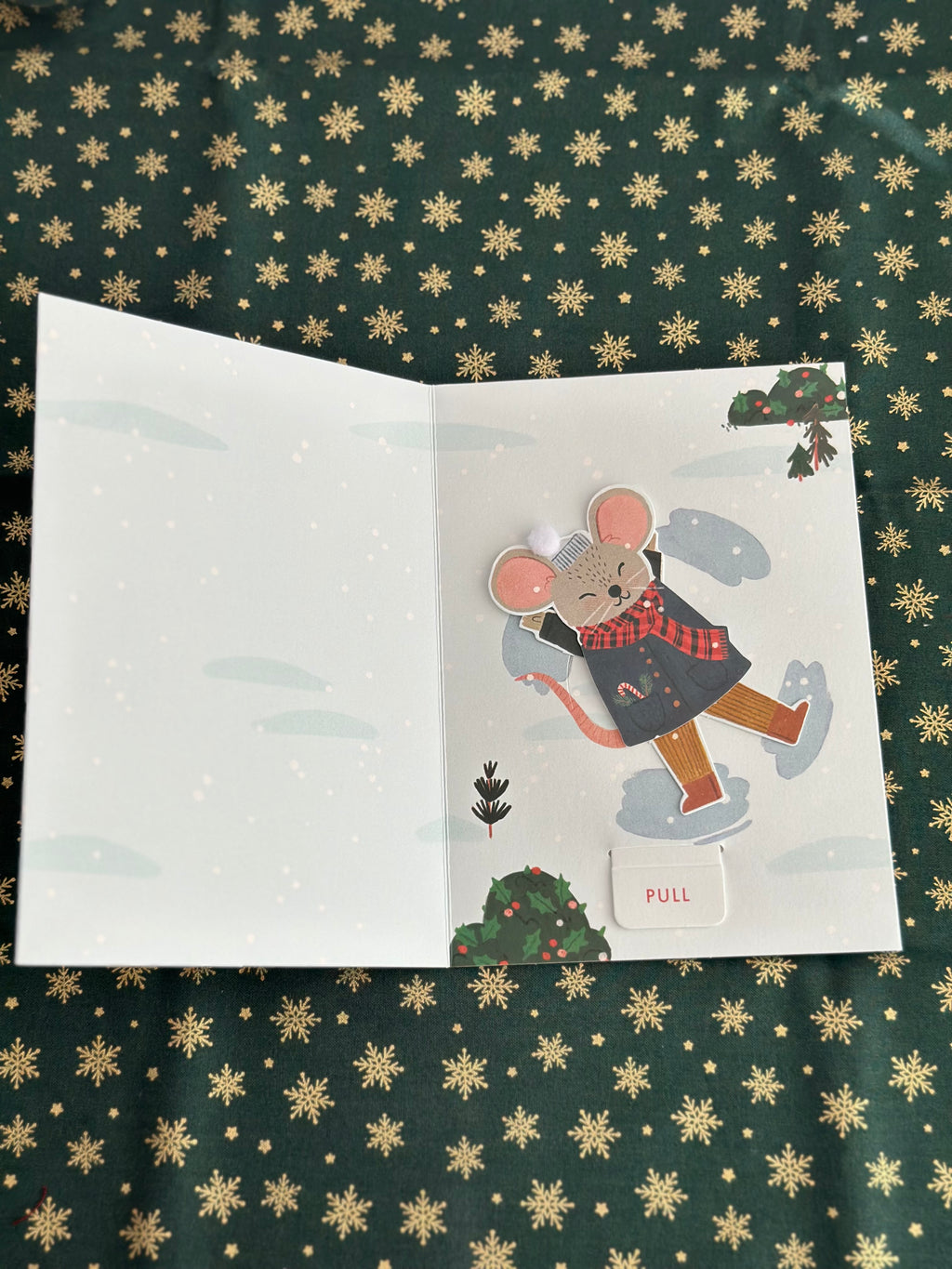 Inside of the holiday card with a smiling mouse character and a pull tab labeled “PULL” in a snowy scene.