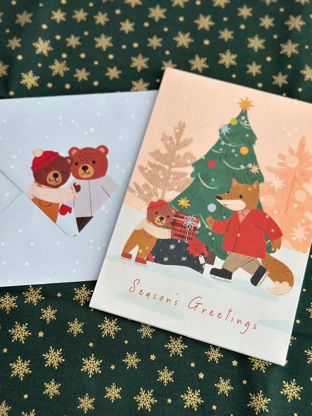 Season’s Greetings card next to blue envelope printed with two bears in scarves and snow.