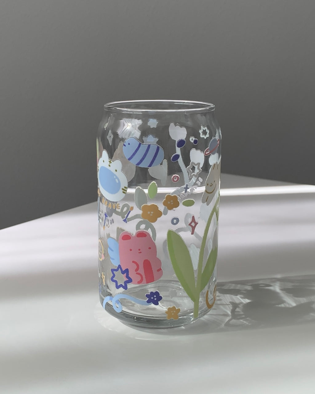Clear 16 oz glass can featuring subtle affirmation phrases and pastel doodle illustrations, styled in soft natural light.
