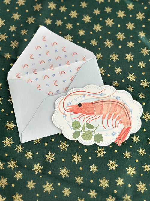 Holiday shrimp greeting card with scalloped edge and blue envelope; shrimp-pattern liner; green fabric with gold snowflakes.