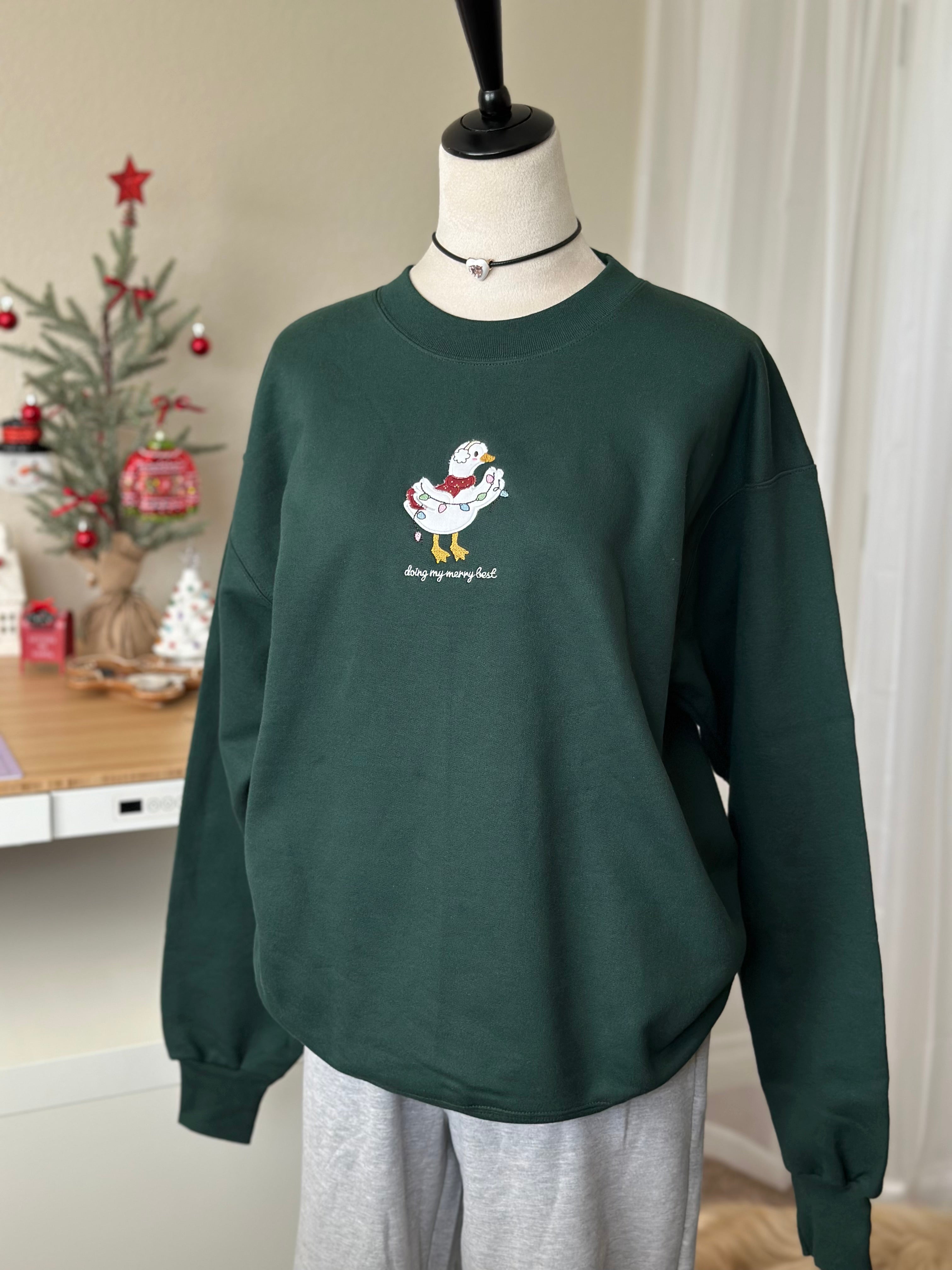Angled view of a forest green Christmas sweatshirt featuring detailed silly goose embroidery with holiday lights