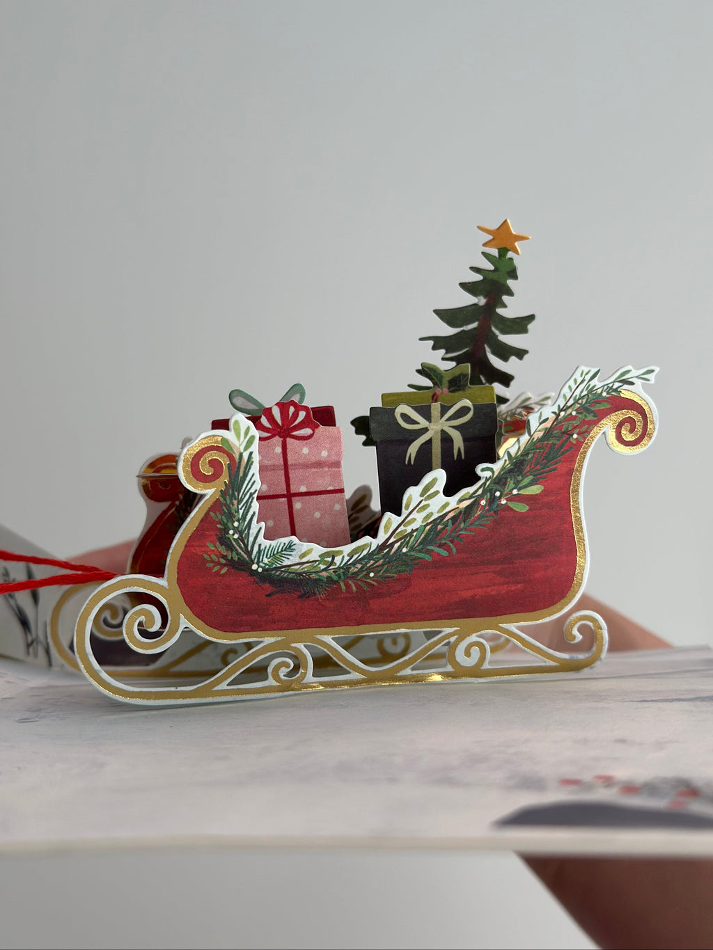Side view of red sleigh with gold accents and presents from pop-up Christmas card.