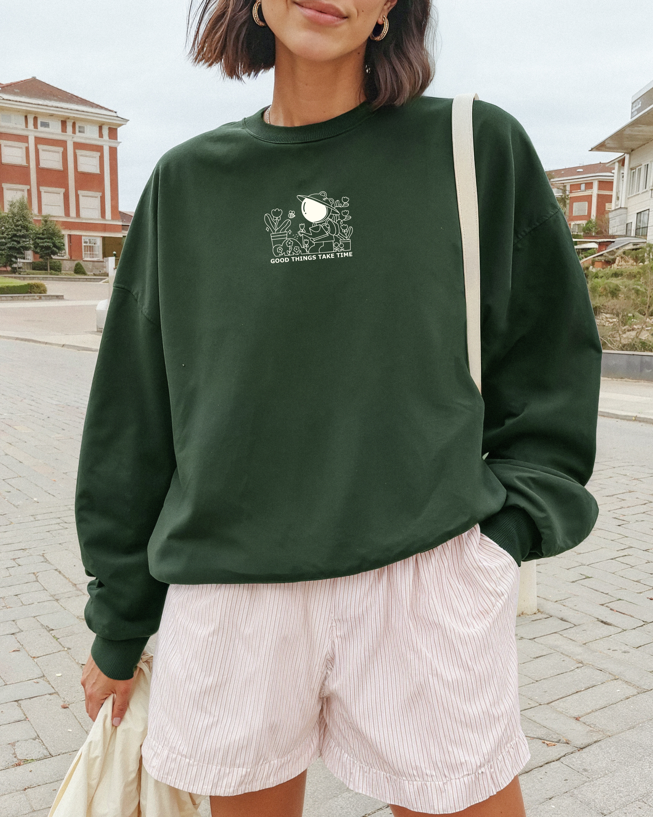 Woman wearing a forest green “Good Things Take Time” embroidered sweatshirt outdoors, styled for slow living and everyday comfort.