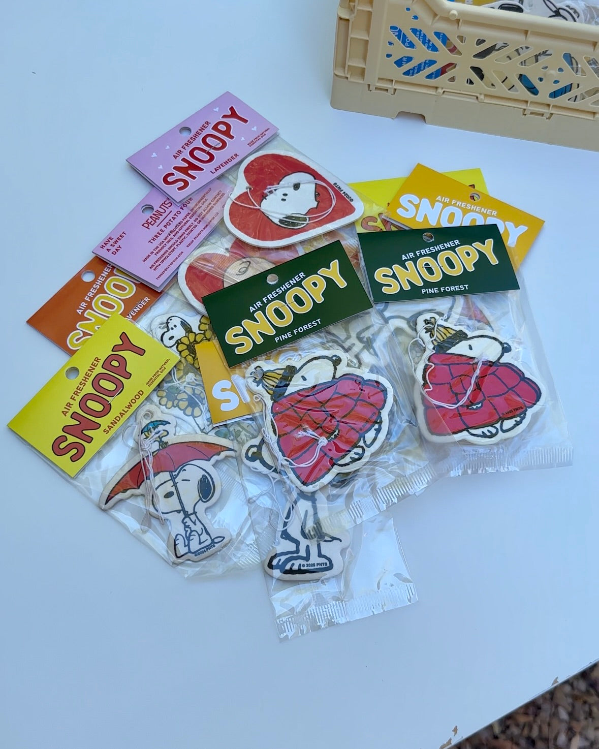 Multiple Snoopy air fresheners in assorted scents and designs, including puffer jacket Snoopy, displayed on a white table.