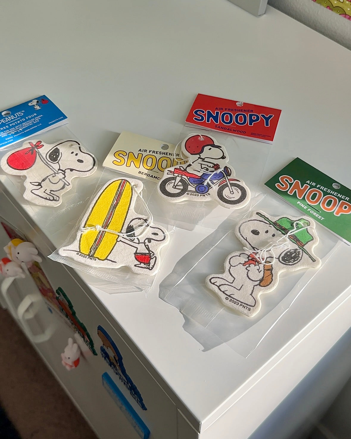 Flatlay of Snoopy air fresheners including Scout Snoopy with pine forest scent. A fun mix of Peanuts designs, perfect for car decor or gifting.