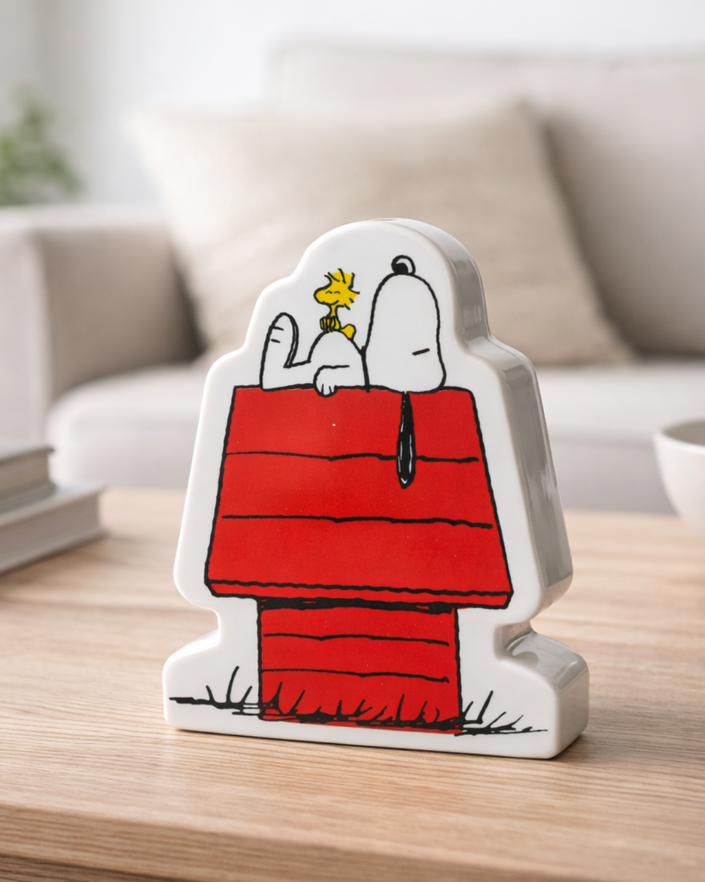 Ceramic Snoopy piggy bank on coffee table with cozy living room background, nostalgic retro cartoon decor and collectible coin bank