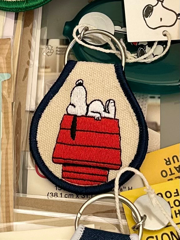 Embroidered Snoopy lying on red doghouse keychain, cream canvas with navy trim.