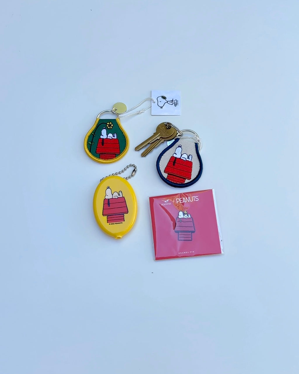 Snoopy Peanuts embroidered keychain and accessories featuring Snoopy napping on his red doghouse, including patch keychains, coin pouch, and enamel pin on white background.