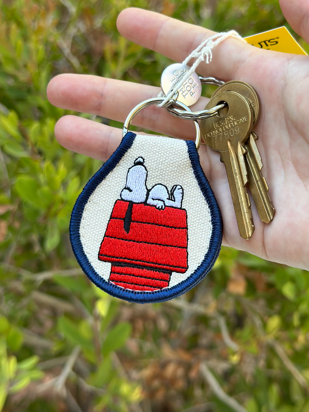 Close-up of Snoopy Peanuts embroidered doghouse keychain with navy trim, attached to a set of keys.