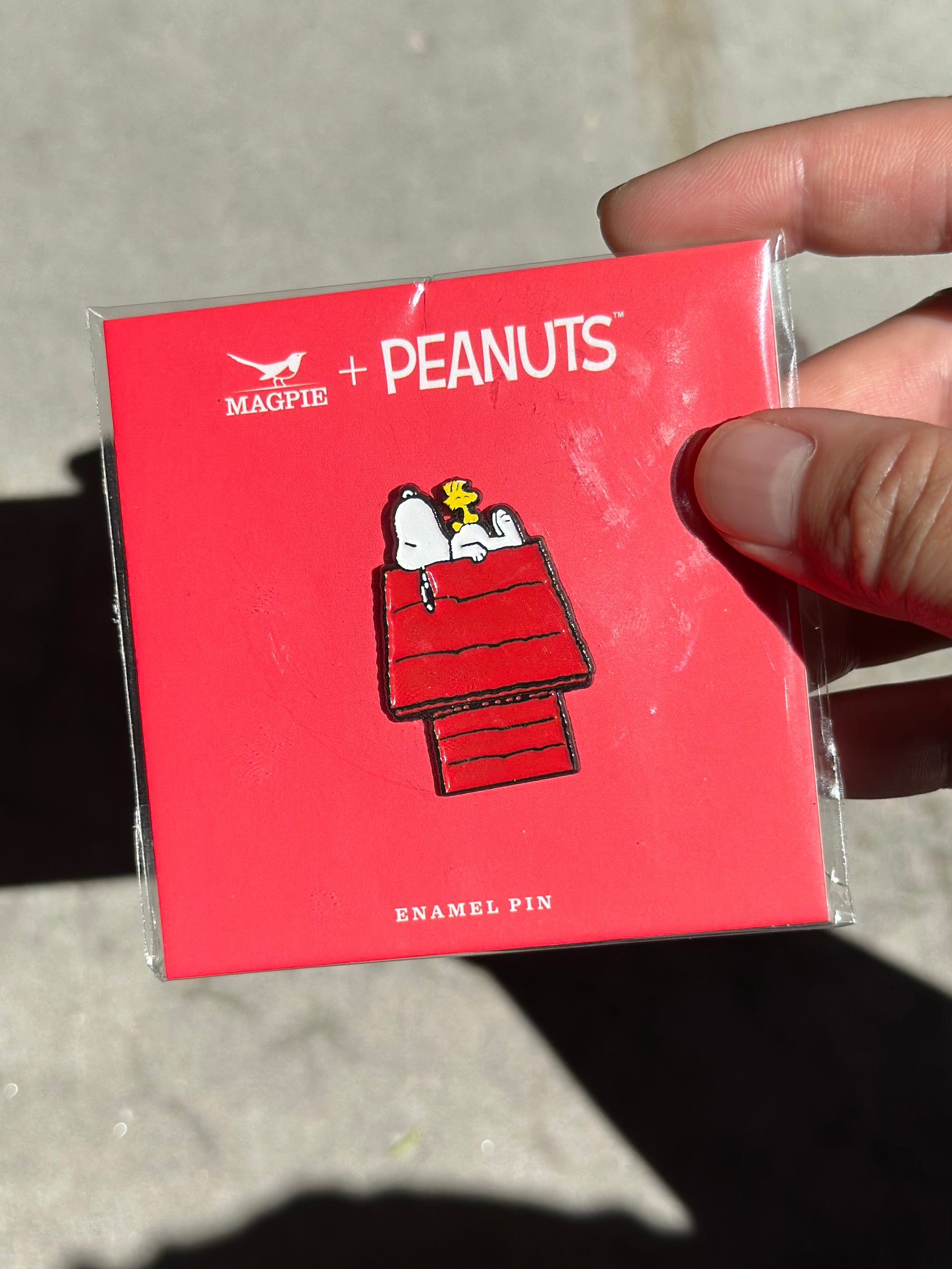 Snoopy and Woodstock enamel pin on red Peanuts® card, photographed in sunlight