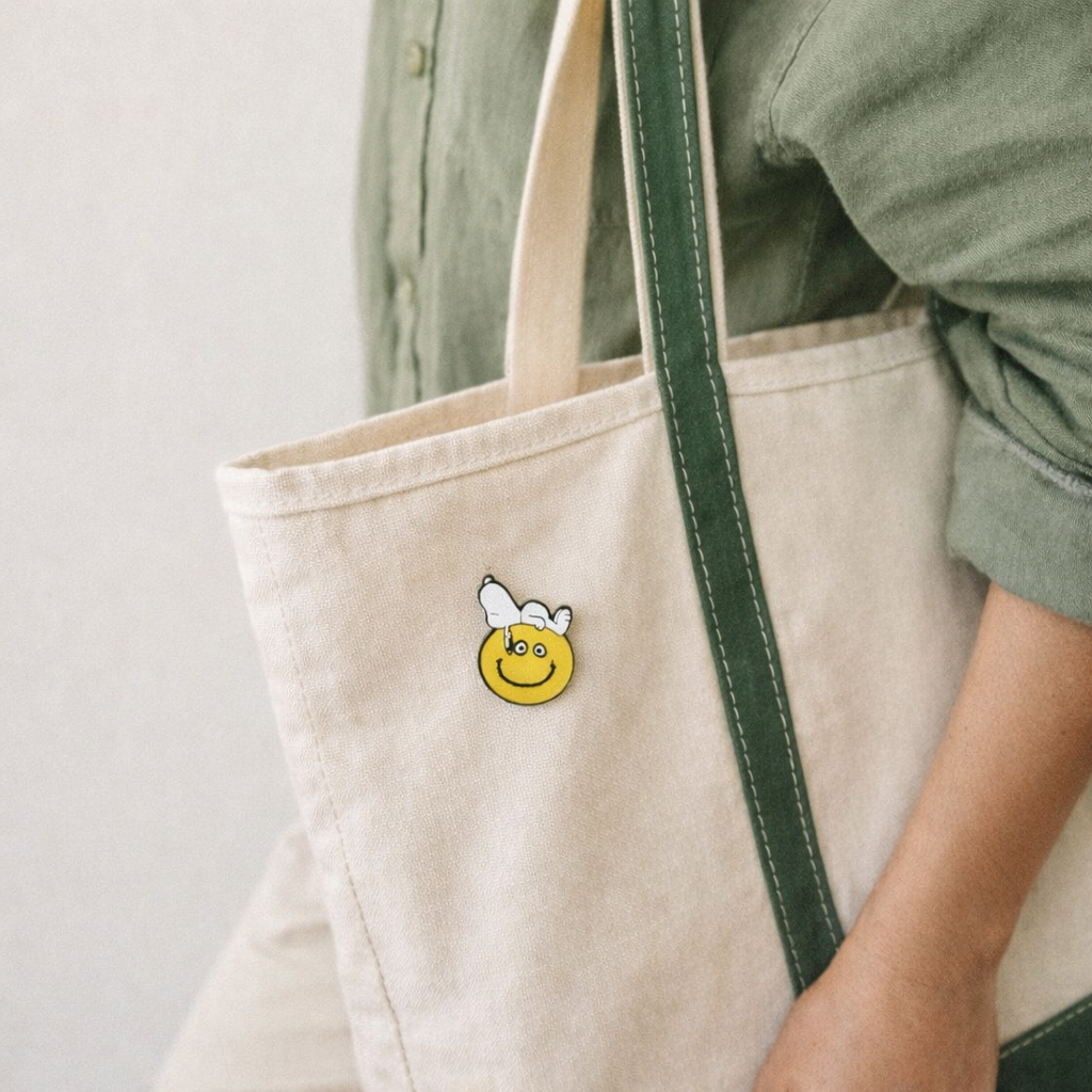 Snoopy smiley enamel pin on a canvas tote bag, cute Peanuts accessory for aesthetic outfits and pin collections.