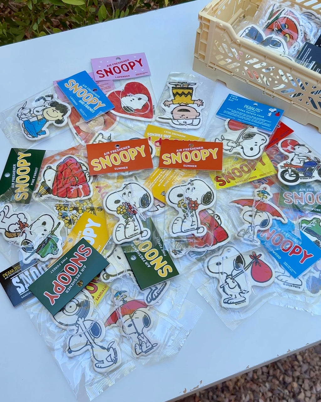 Flatlay display of multiple Snoopy “Flower Bouquet” Summer air fresheners with bright orange packaging, surrounded by other Peanuts® character designs, perfect for car or home.