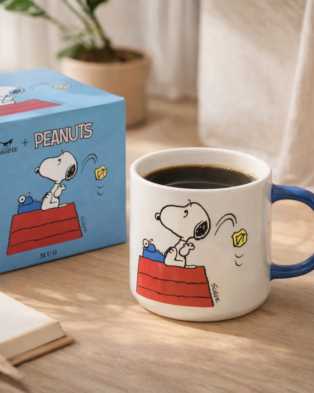 Snoopy Genius at Work ceramic mug with coffee on a wooden desk beside the Peanuts collector box, cozy morning coffee setup for writers, students, and Snoopy fans