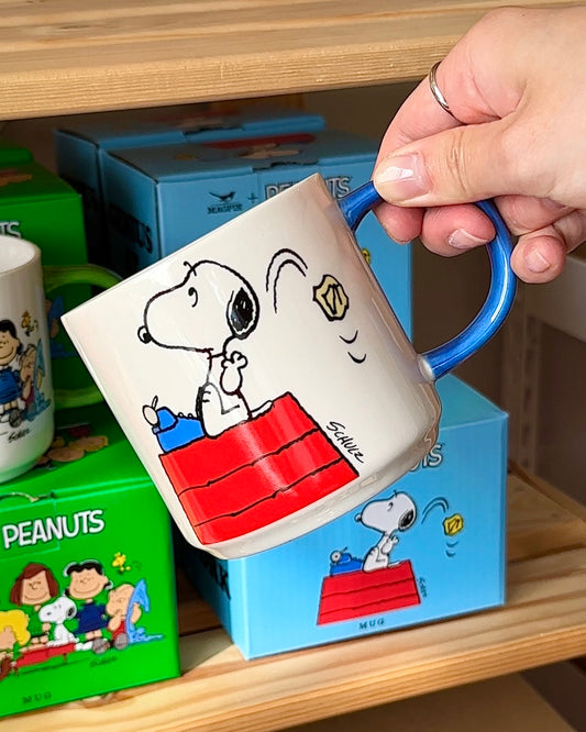 Person holding Snoopy “Genius at Work” mug in front of Peanuts® gift box
