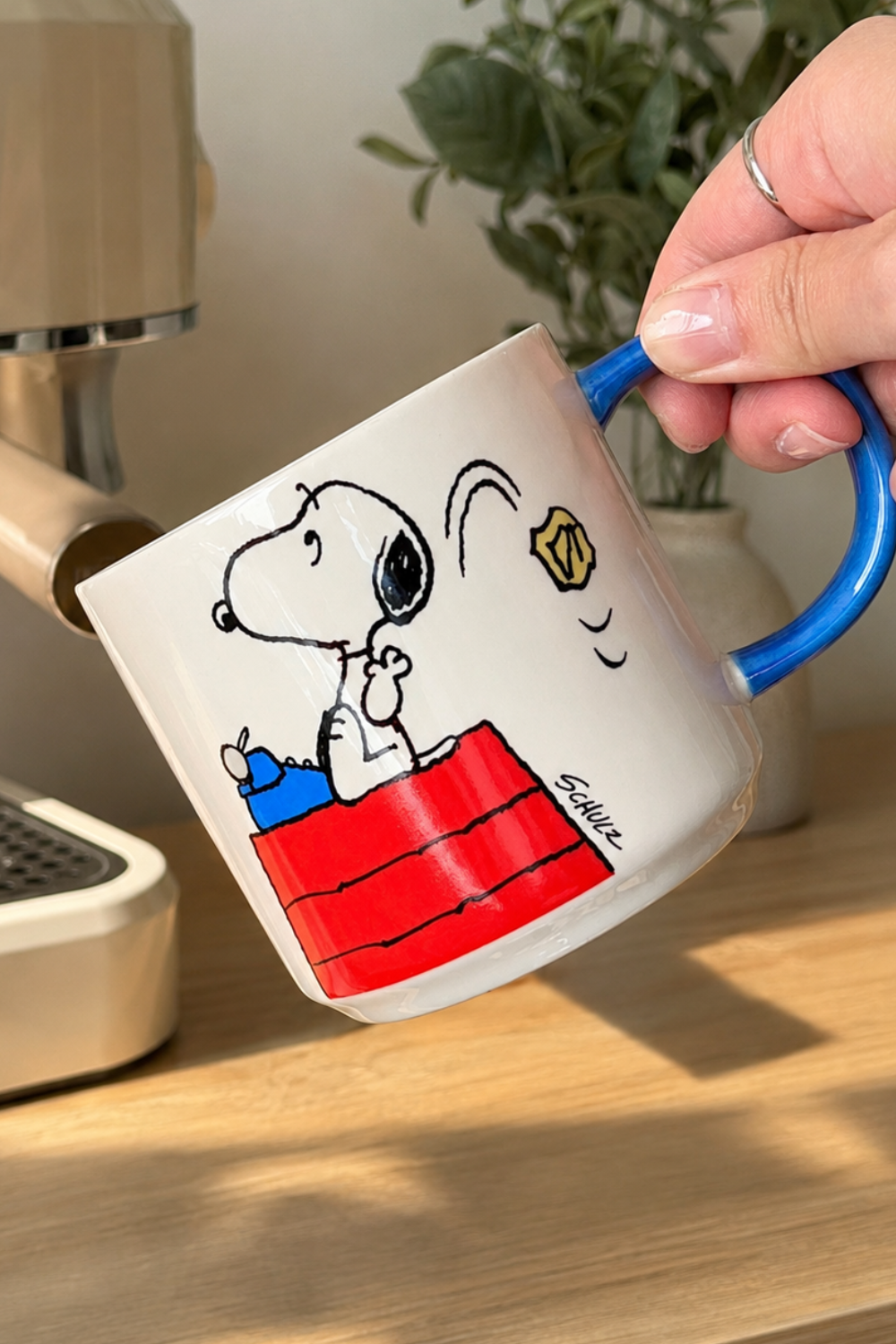 Snoopy Genius at Work coffee mug with blue handle displayed in a bright coffee station.