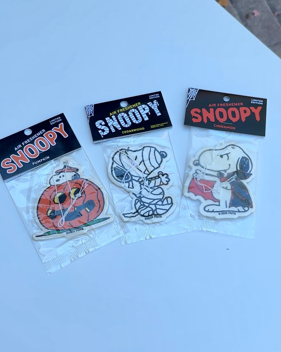 Three-pack of Snoopy Halloween air fresheners featuring pumpkin, mummy, and vampire designs, displayed on a white table.