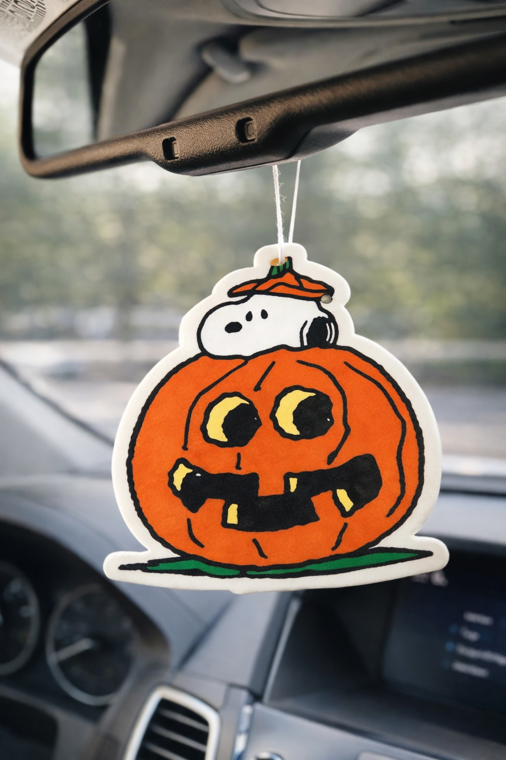 Snoopy Halloween pumpkin car air freshener hanging from rearview mirror, cute Peanuts Halloween car decor accessory.
