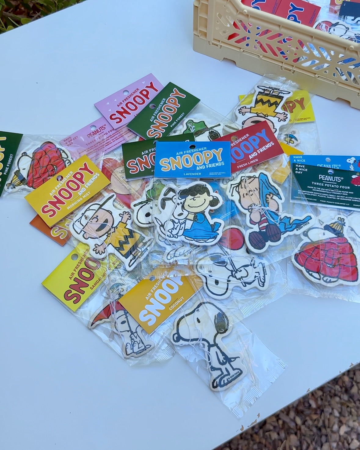 Flat lay of assorted Snoopy and Peanuts® character air fresheners, featuring Snoopy & Lucy Hug lavender scent in the center.