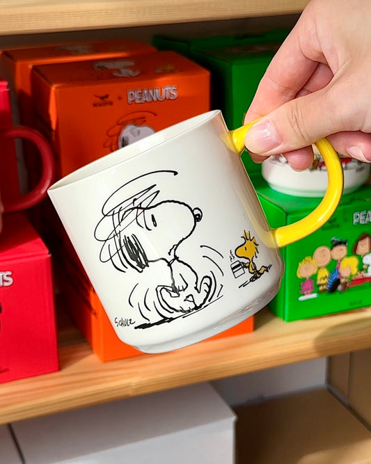 Hand holding Snoopy mug with yellow handle and morning coffee design