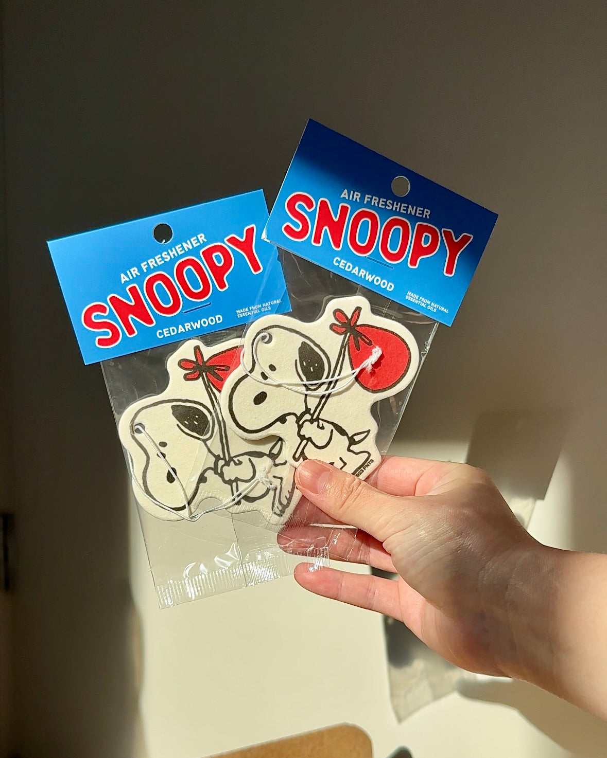 Snoopy Nomad air freshener with red bindle, held up in sunlight in blue Cedarwood packaging