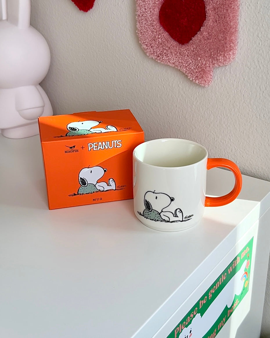 Peanuts Snoopy ceramic mug with orange handle shown next to collector box, minimalist Snoopy artwork on white coffee mug.