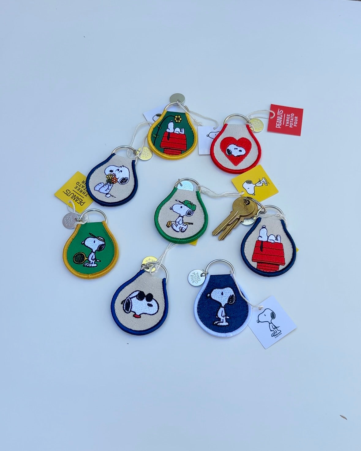 Collection of Snoopy Peanuts embroidered keychains in assorted colors and designs, featuring tennis Snoopy, sunglasses Snoopy, and Snoopy on his doghouse.