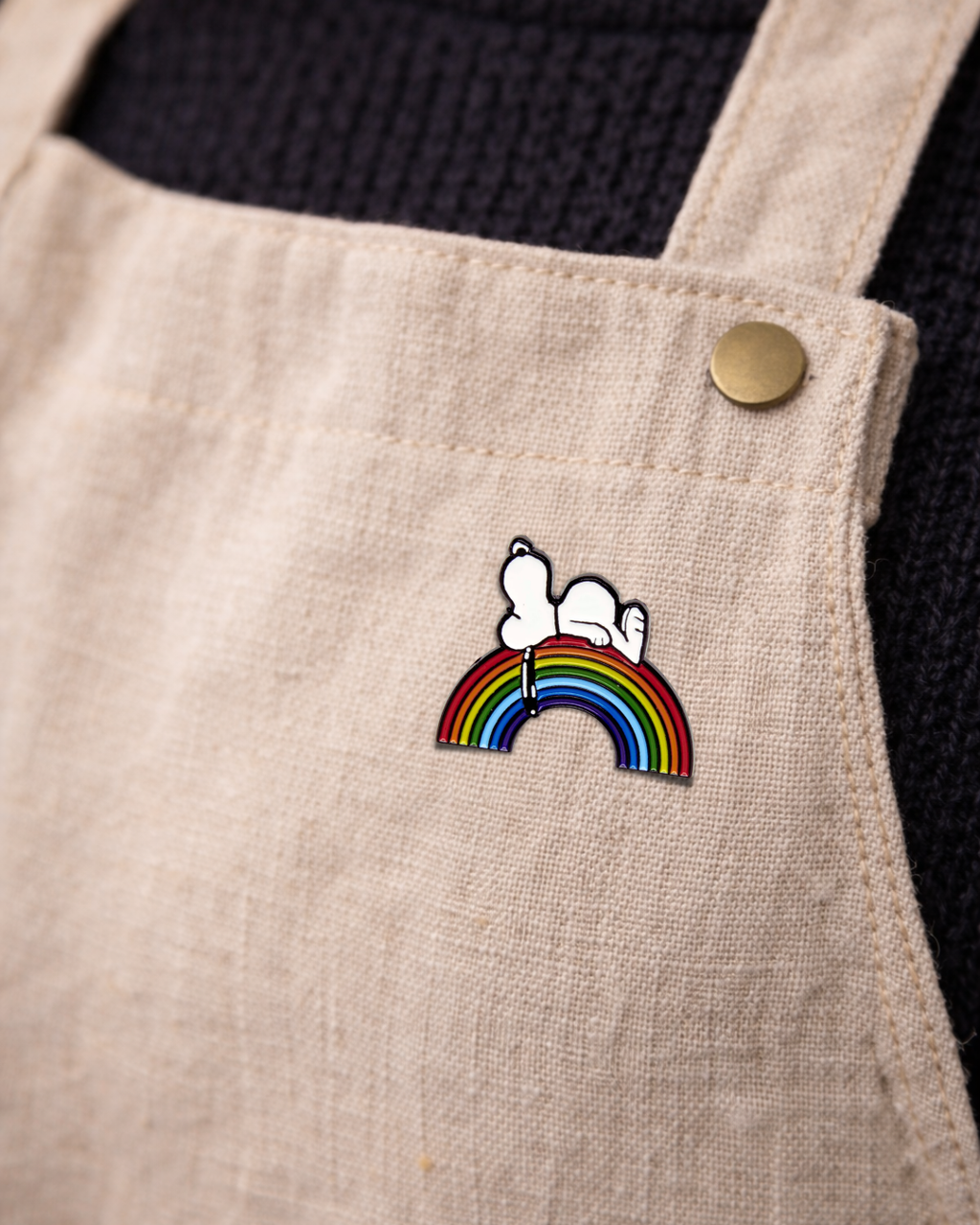 Snoopy rainbow enamel pin on cream overalls, colorful Peanuts accessory for outfits, backpacks, and enamel pin collectors.