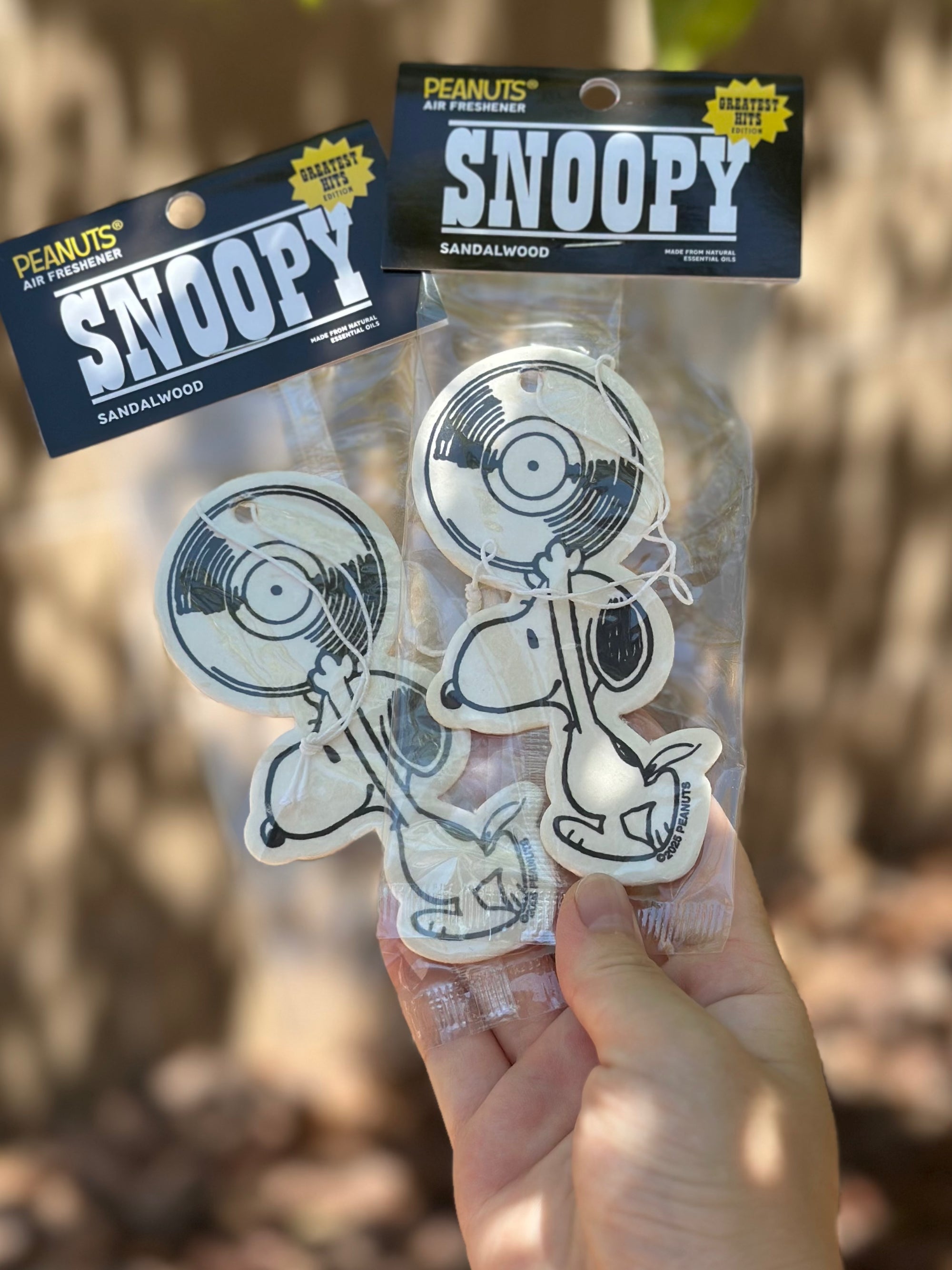 Two packaged Snoopy sandalwood air fresheners featuring Snoopy holding a vinyl record, displayed outdoors in natural light.