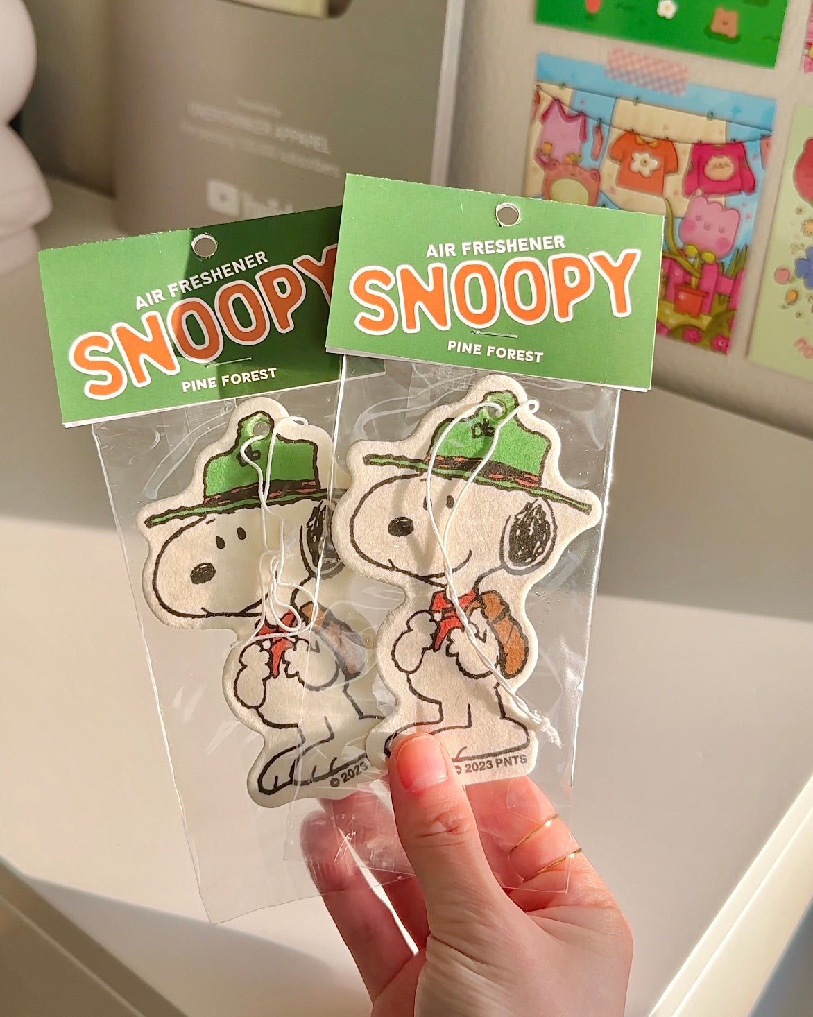 Scout Snoopy Pine Forest air freshener held in hand. Cute vintage-style Peanuts design for cars or dorms with woodsy summer scent.