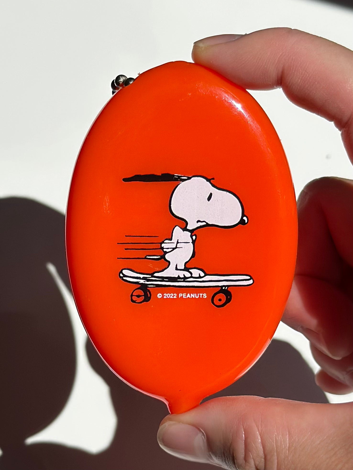 Bright orange Snoopy skateboard coin pouch keychain held in hand with ball chain.