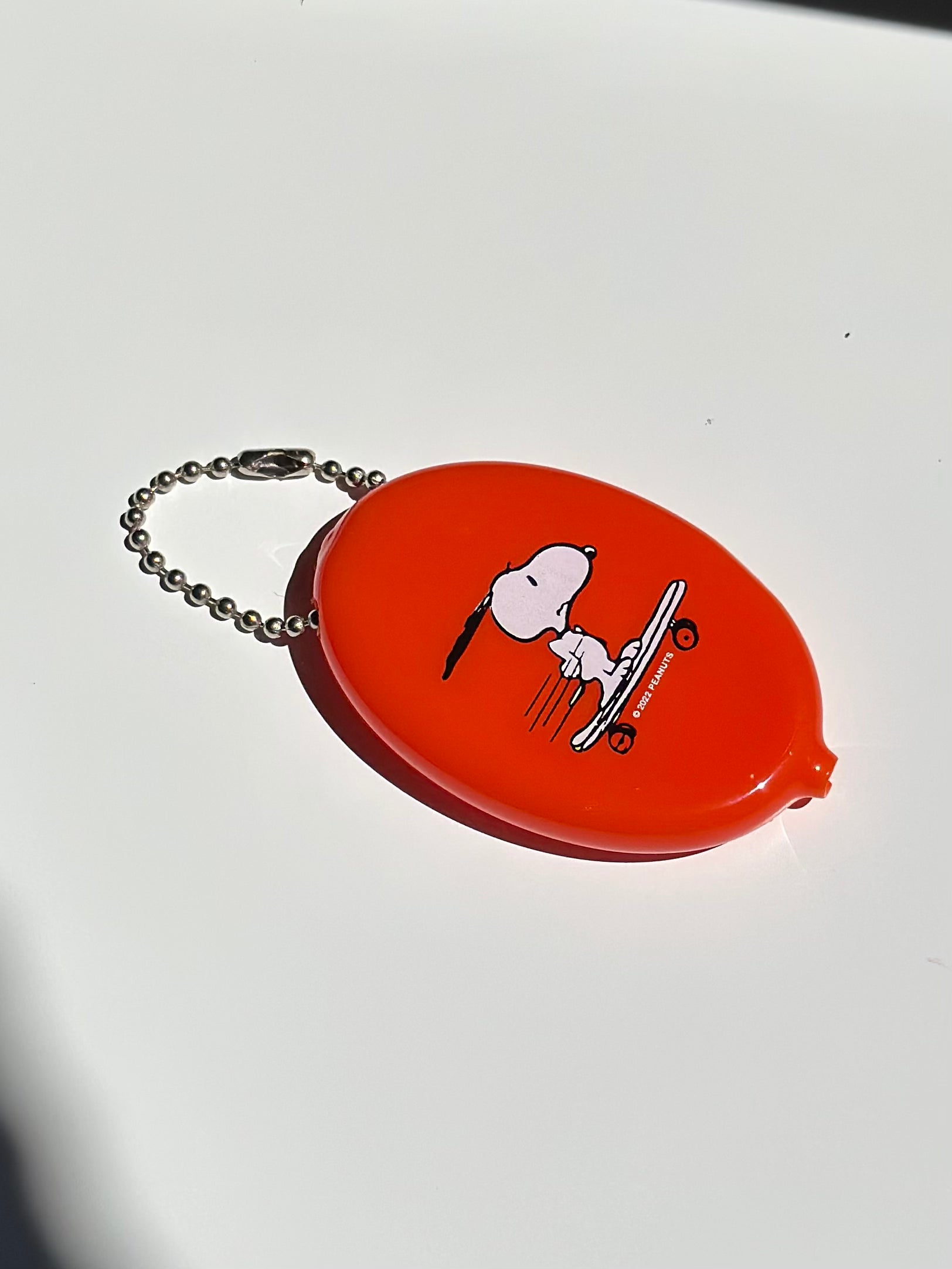 Snoopy skateboard vinyl coin pouch in bold orange with ball chain keyring.