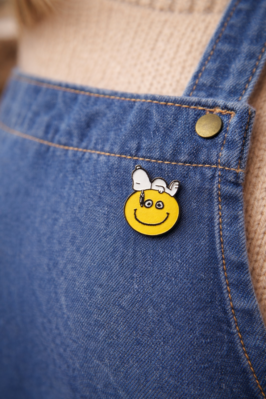 Snoopy smiley enamel pin attached to a denim apron, cute cartoon accessory for outfits and enamel pin collections.