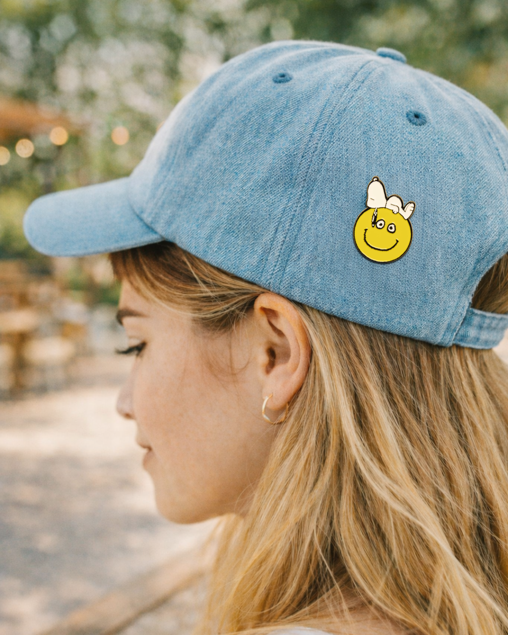 Snoopy smiley face enamel pin on a blue baseball cap, cute Peanuts accessory for pin collectors and cartoon fans.