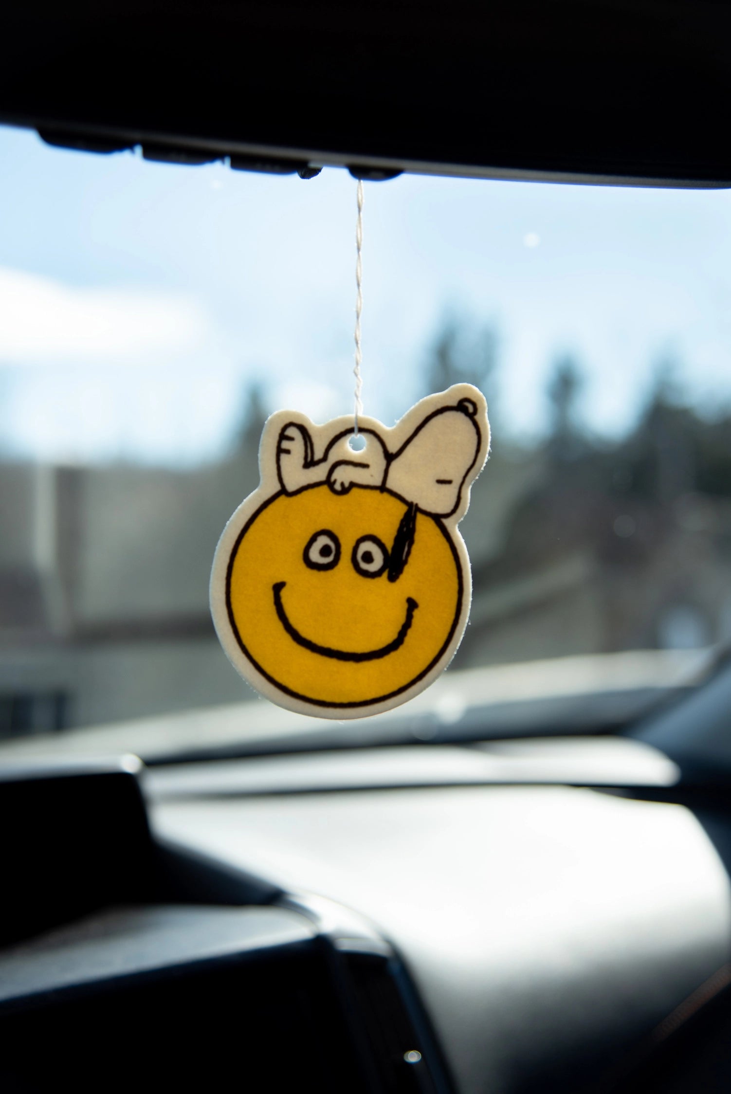 Snoopy air freshener with smiley face design hanging from a rearview mirror. Cozy vanilla-scented decor for cars, dorms, or happy gifting.