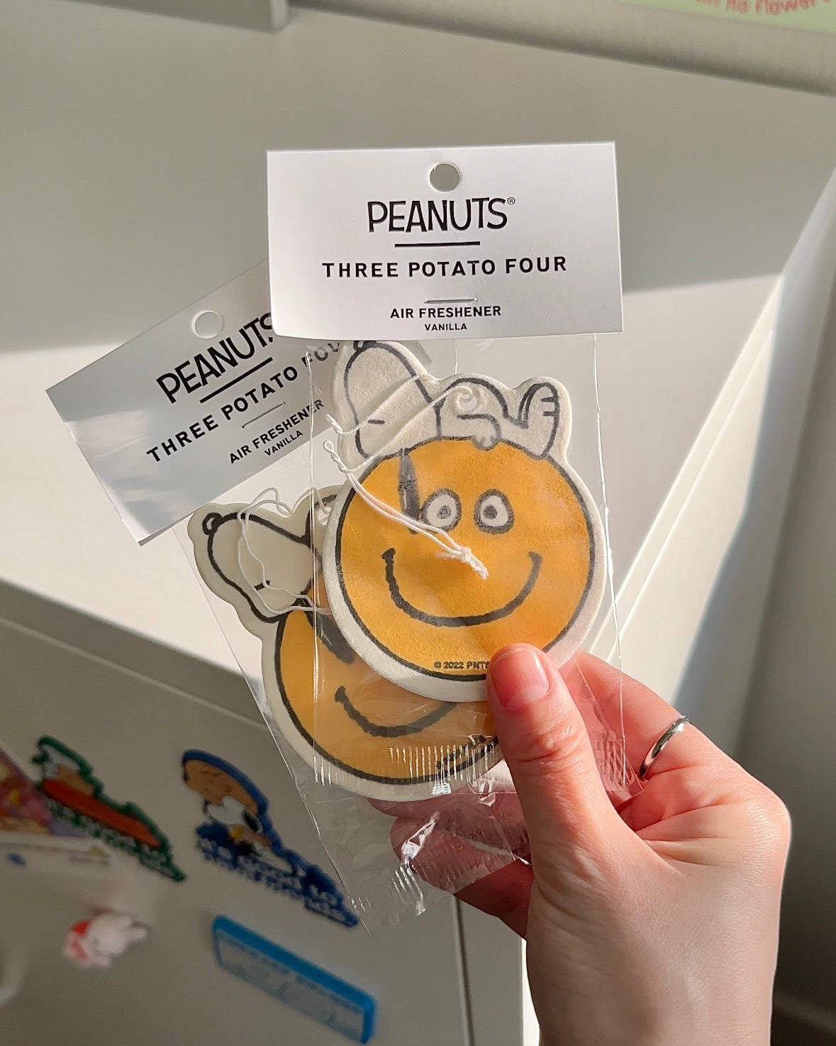 Snoopy smiley face air freshener in hand. French vanilla scented Peanuts accessory for car or cozy decor, eco-friendly and cheerful.