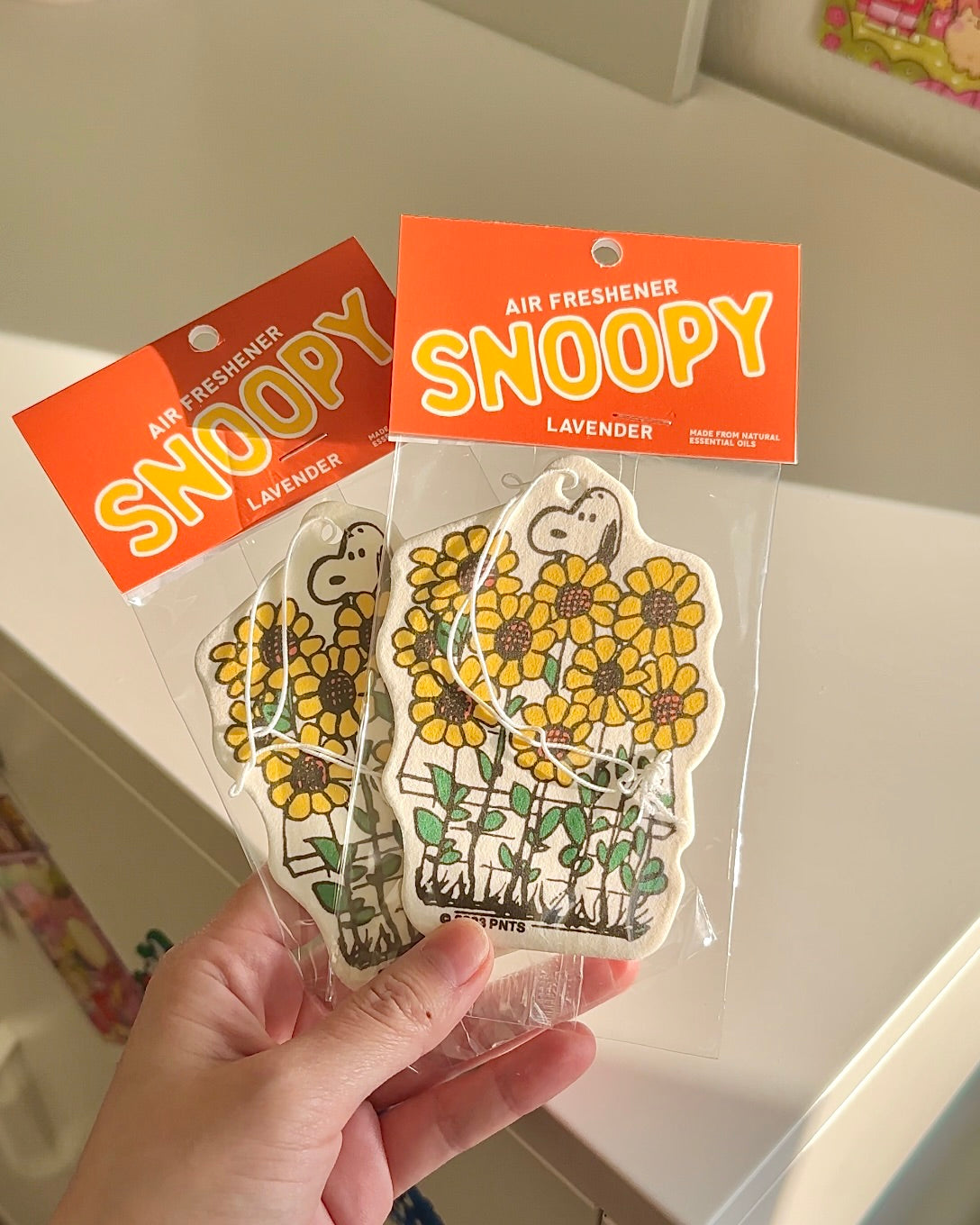 Snoopy sunflower air freshener with calming lavender scent held in hand. Cheerful Peanuts design perfect for summer car decor or gifting.