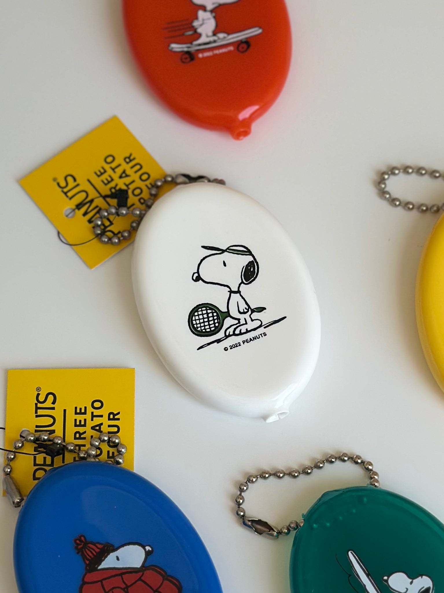 White Snoopy tennis coin pouch surrounded by colorful Peanuts® retro pouches.