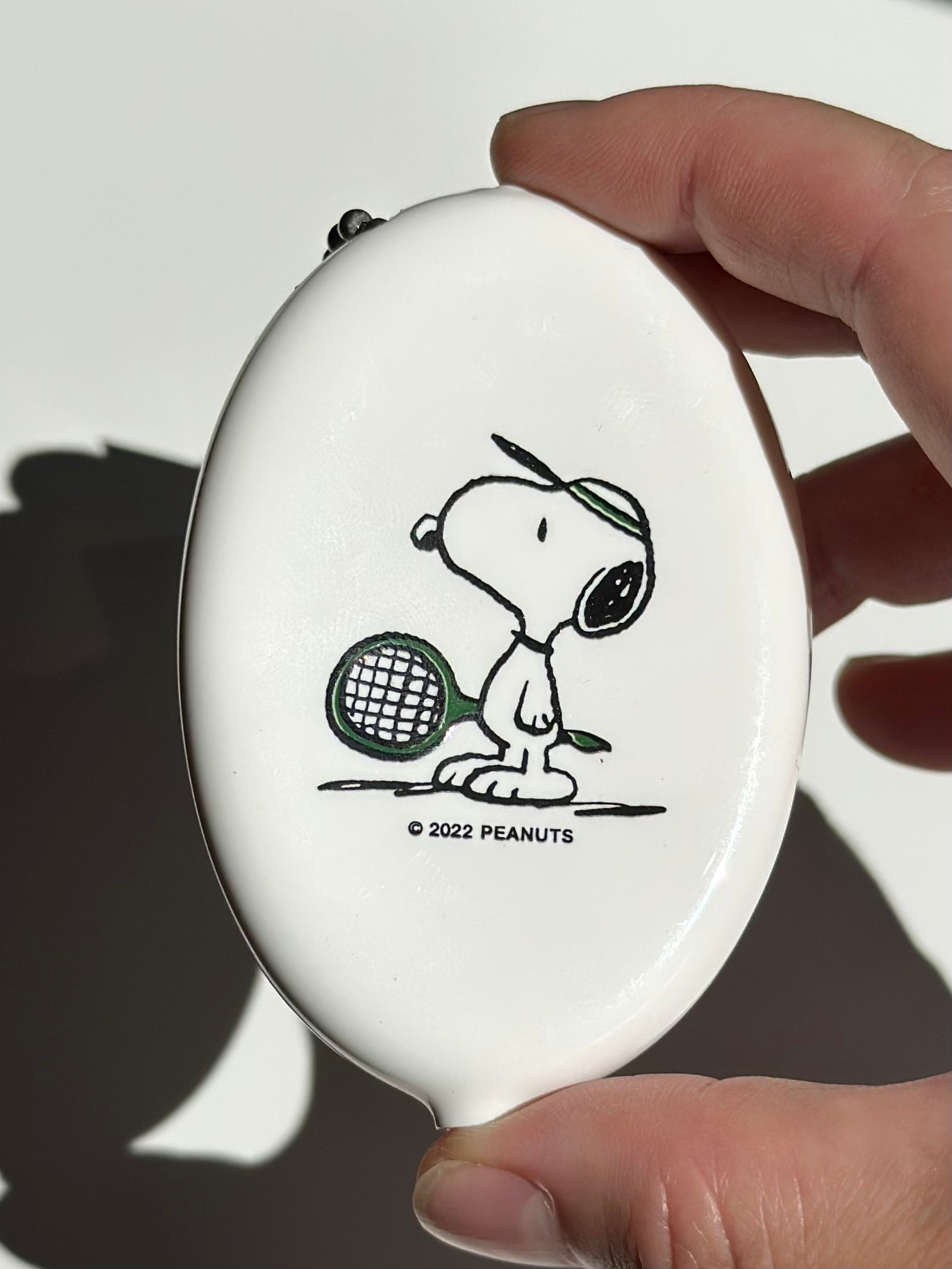 Snoopy tennis coin pouch in creamy white vinyl, held in hand with ball chain keyring.