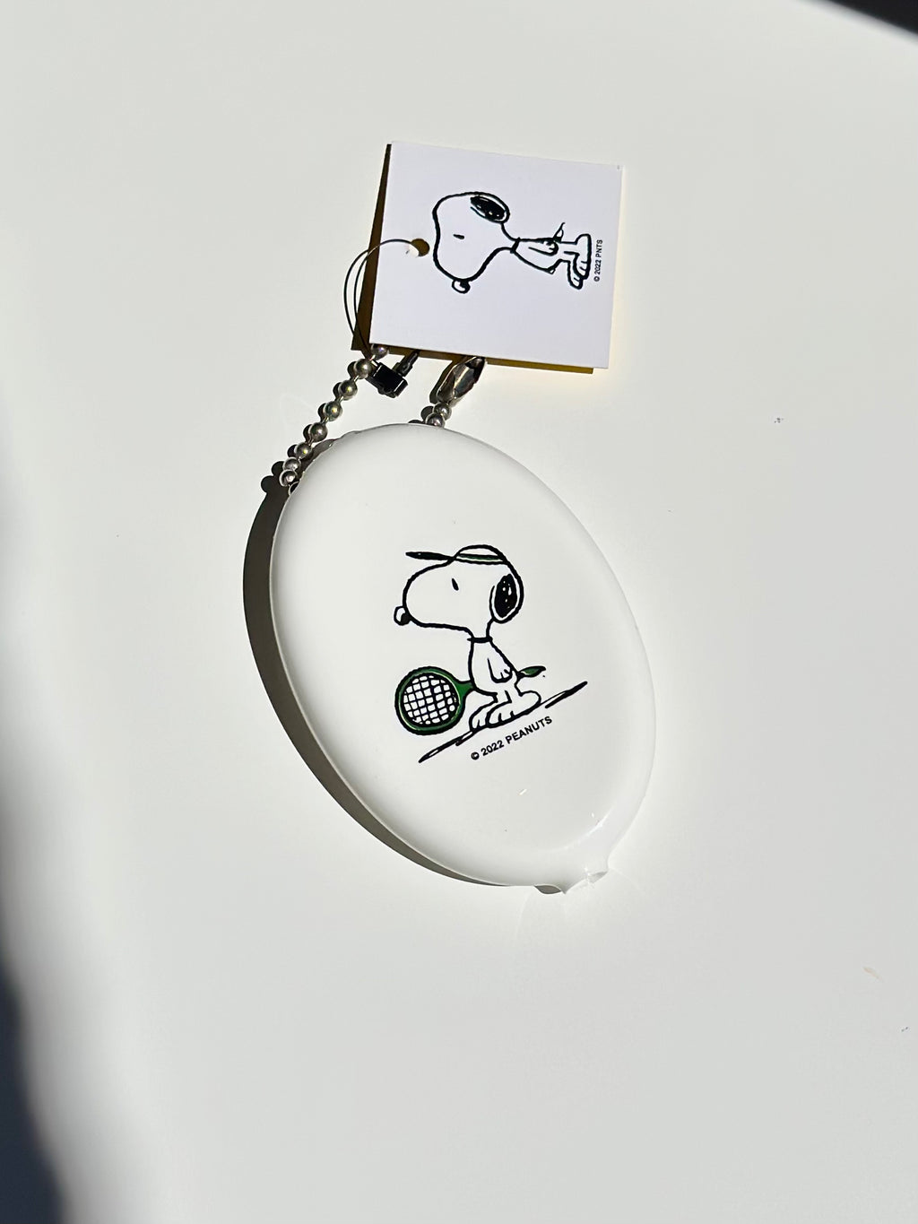 Creamy white Snoopy tennis vinyl coin pouch with ball chain keyring on white backdrop.