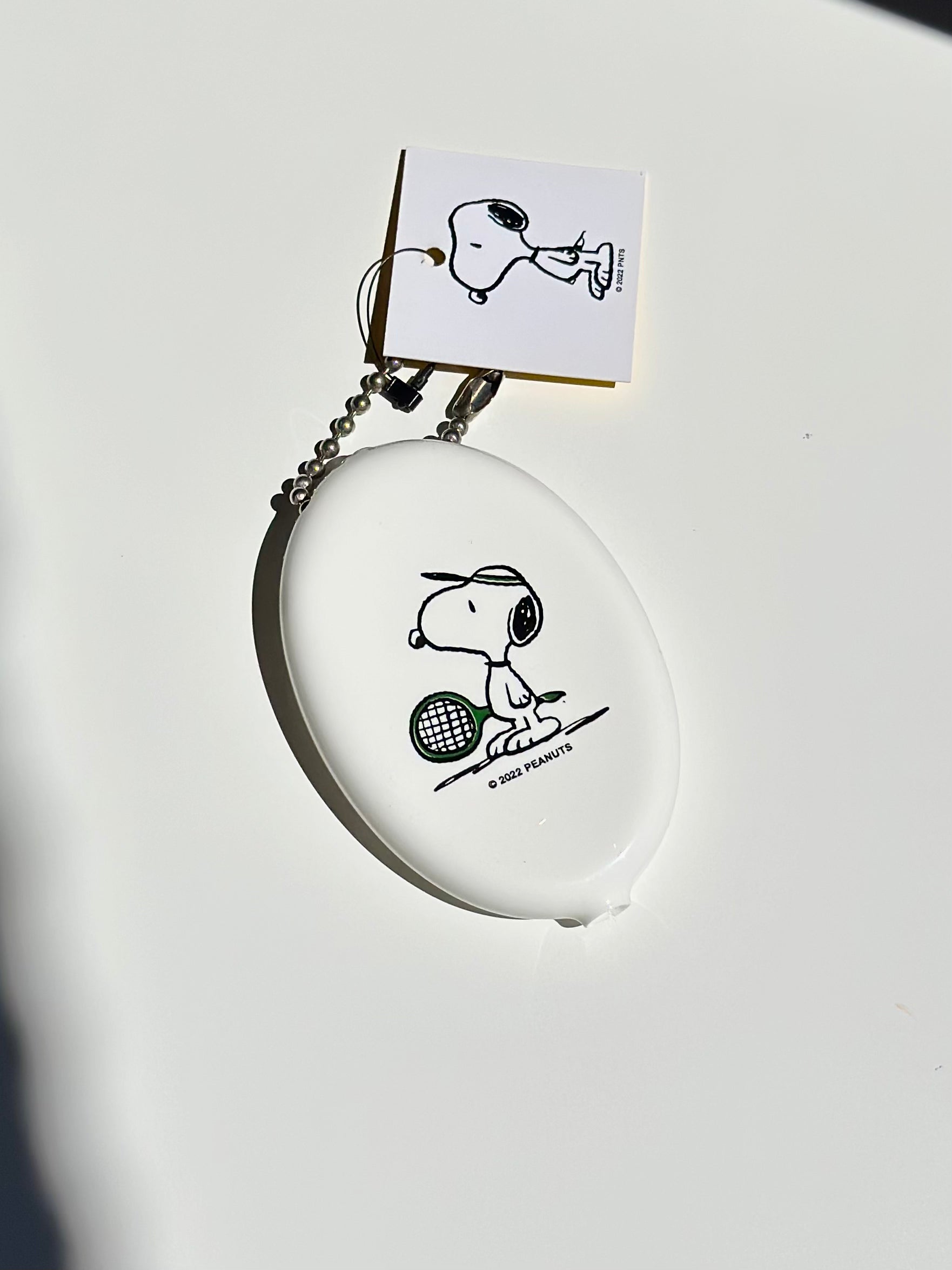 Creamy white Snoopy tennis vinyl coin pouch with ball chain keyring on white backdrop.