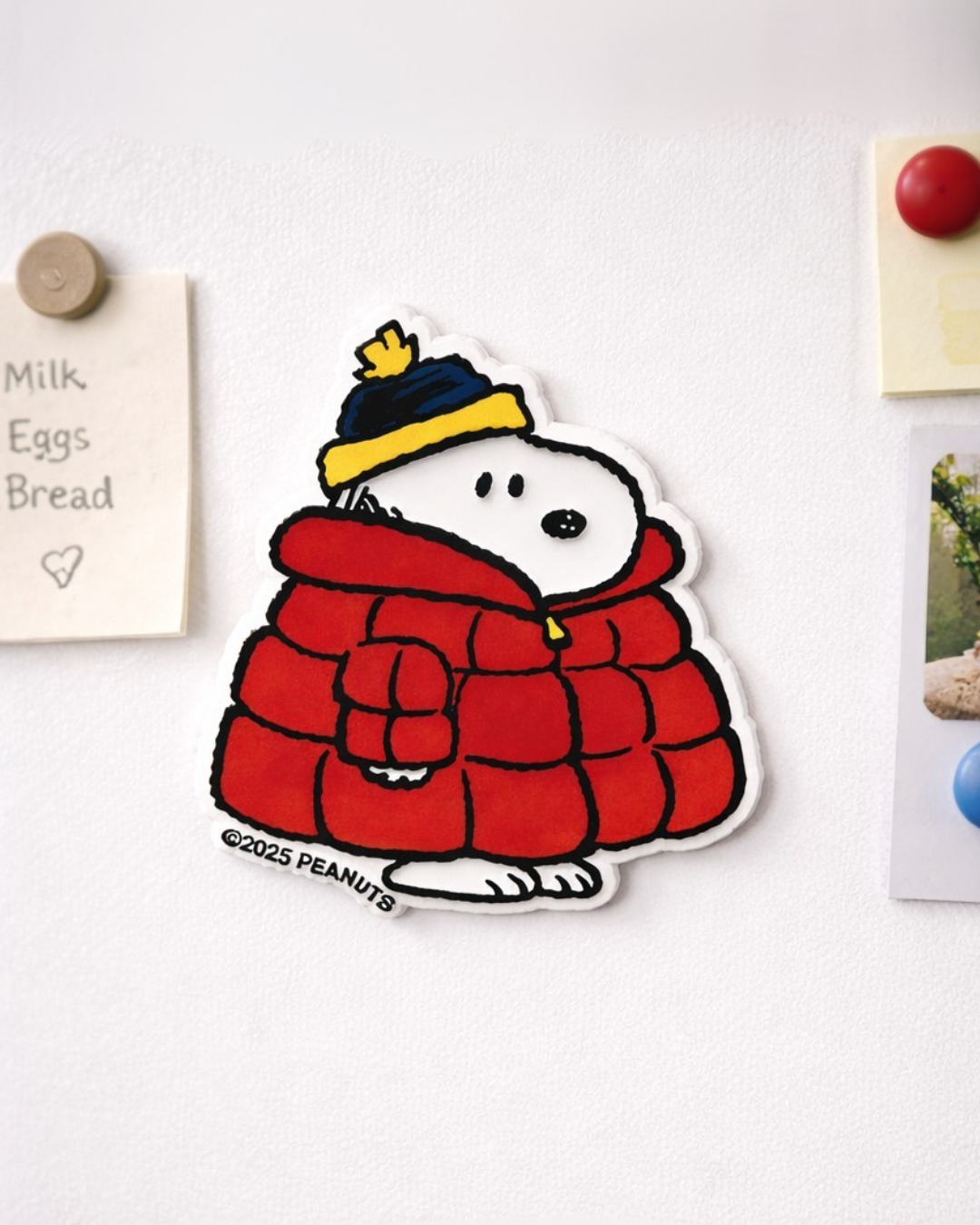 Snoopy winter jacket fridge magnet on a white refrigerator holding a grocery list note, cute Peanuts kitchen magnet decor.