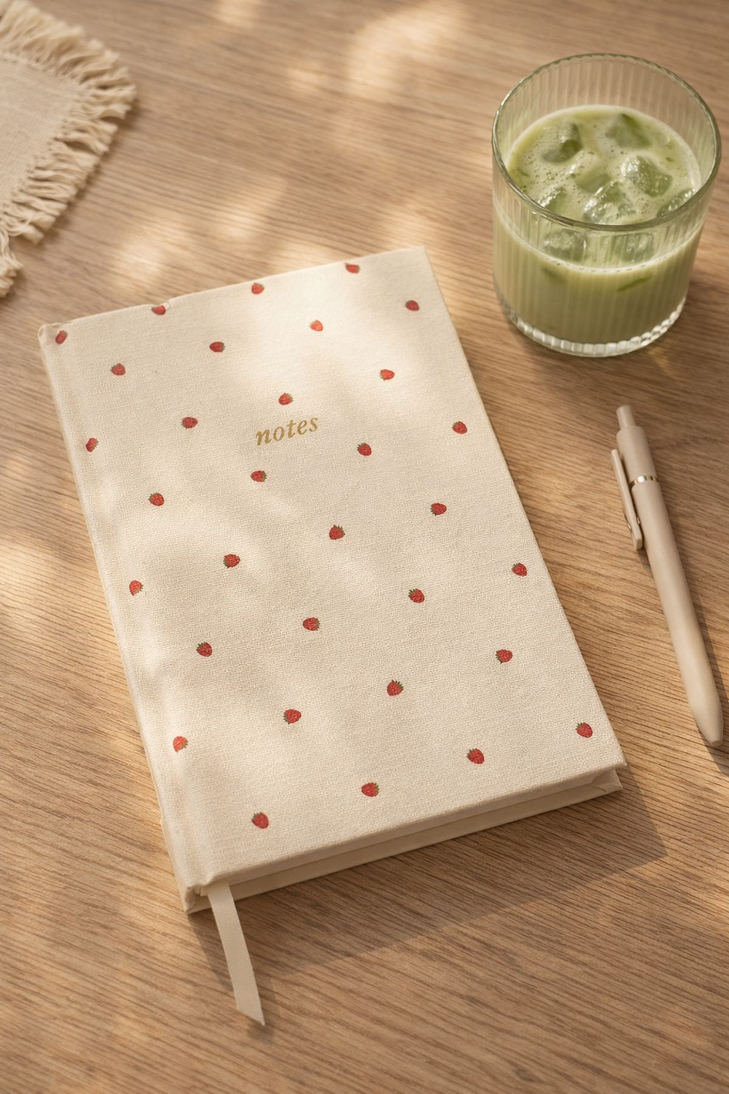 Strawberry aesthetic notebook with cream linen hardcover and gold notes lettering, A5 lined journal styled on wooden desk with pen and iced matcha, cute minimal stationery gift.