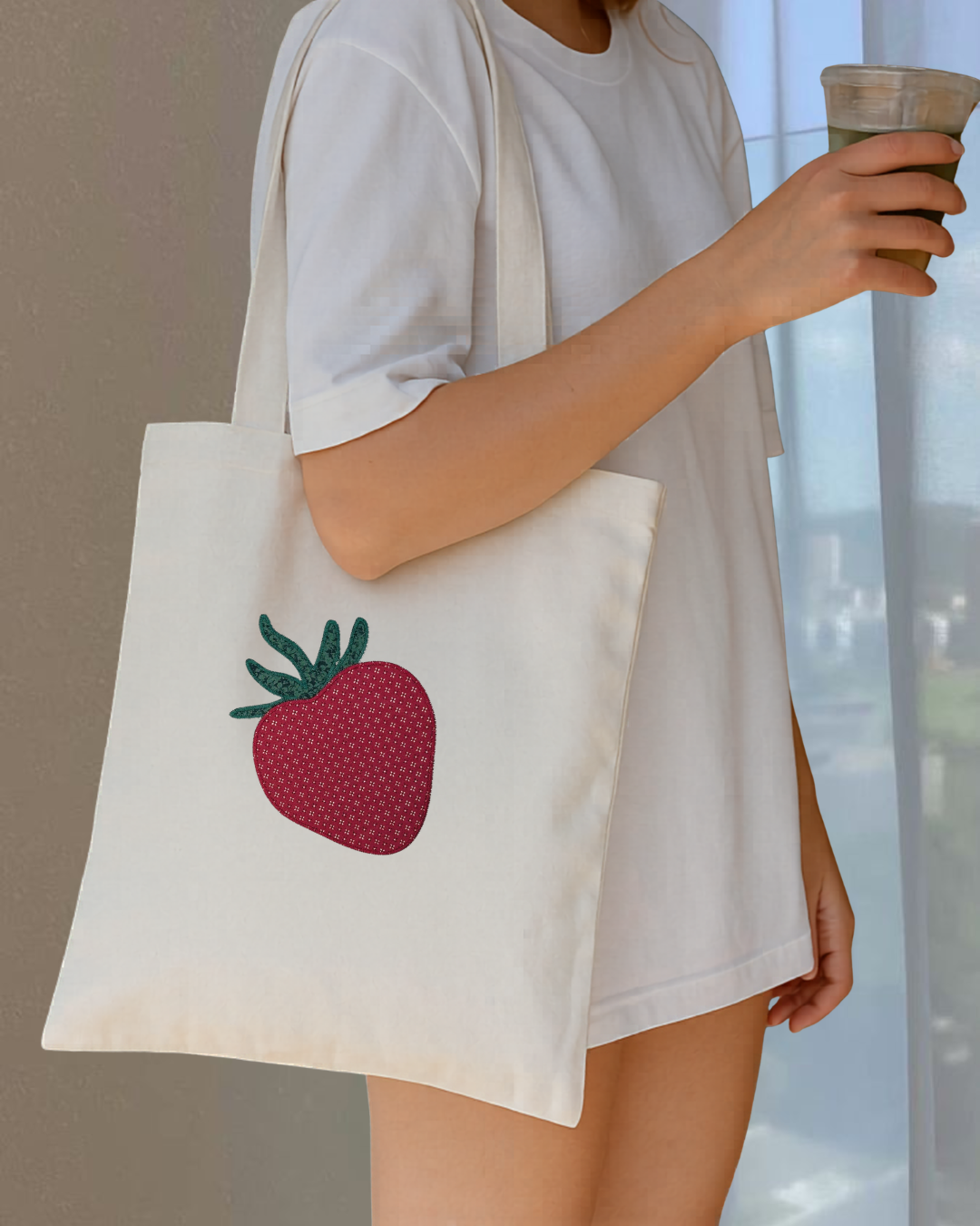 Woman carrying natural canvas strawberry tote bag with embroidered gingham design, casual everyday outfit with reusable cotton tote