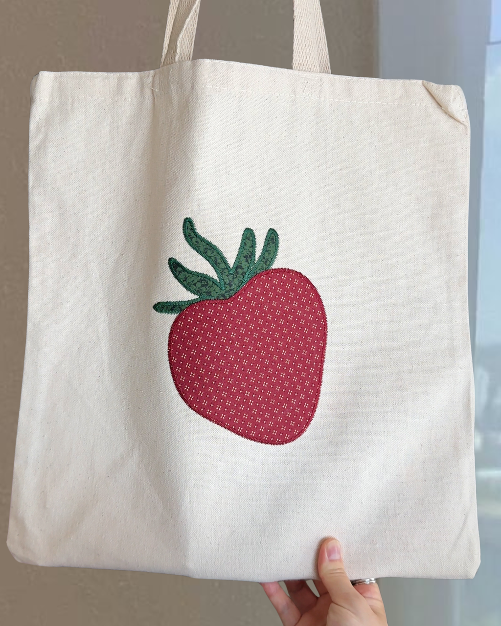 Close up of strawberry embroidery on natural canvas tote bag showing gingham fabric detail and stitched texture