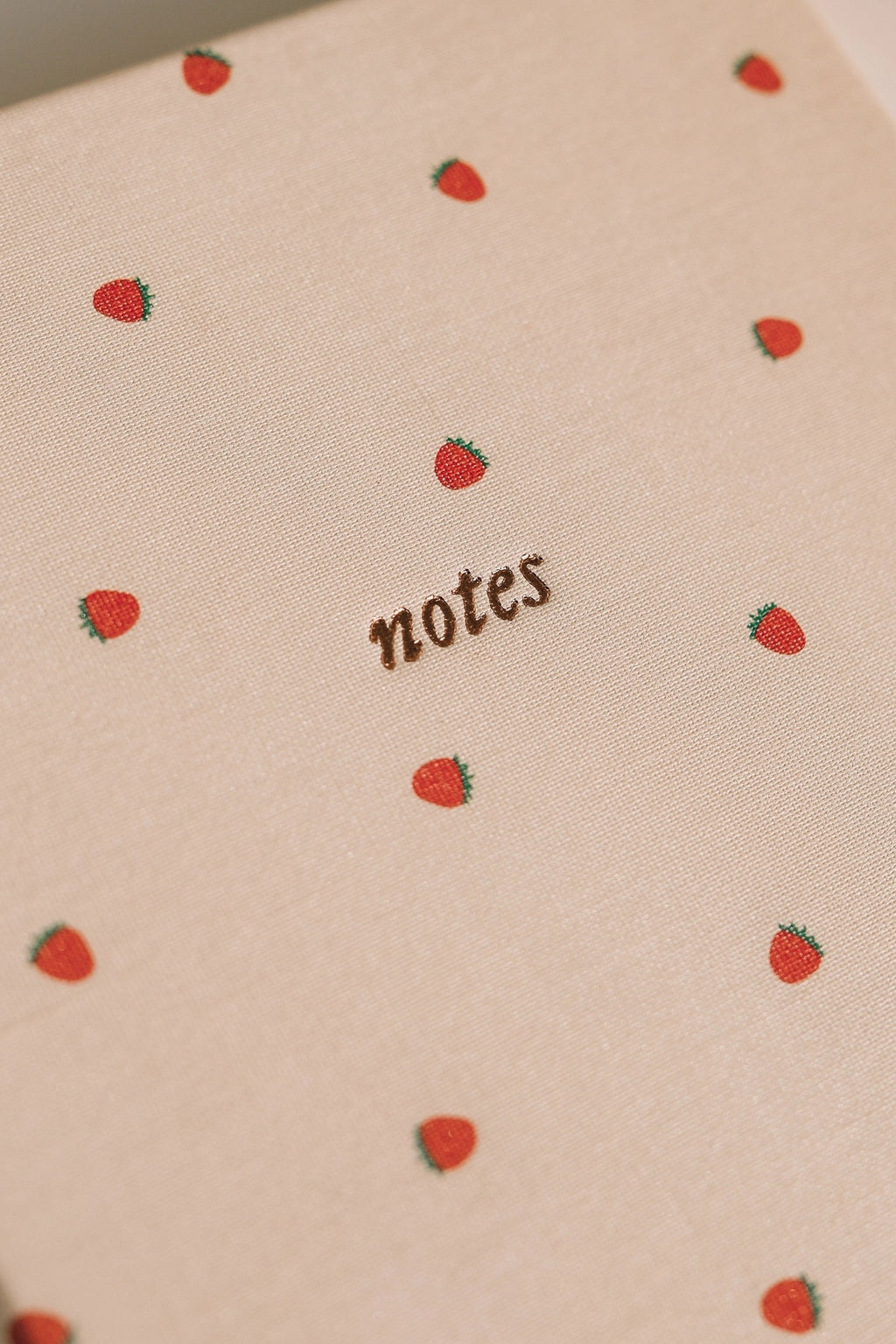 Close-up of strawberry-patterned linen notebook cover with gold “notes” text, minimalist stationery journal for writing and journaling.