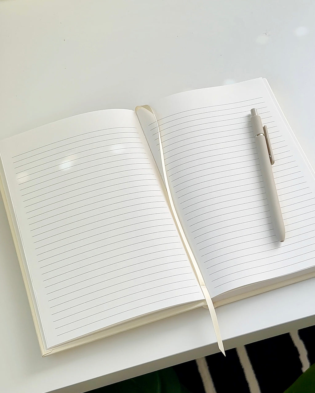 Open A5 strawberry linen journal with cream lined pages, a ribbon bookmark, and a pen resting on a clean desk surface.