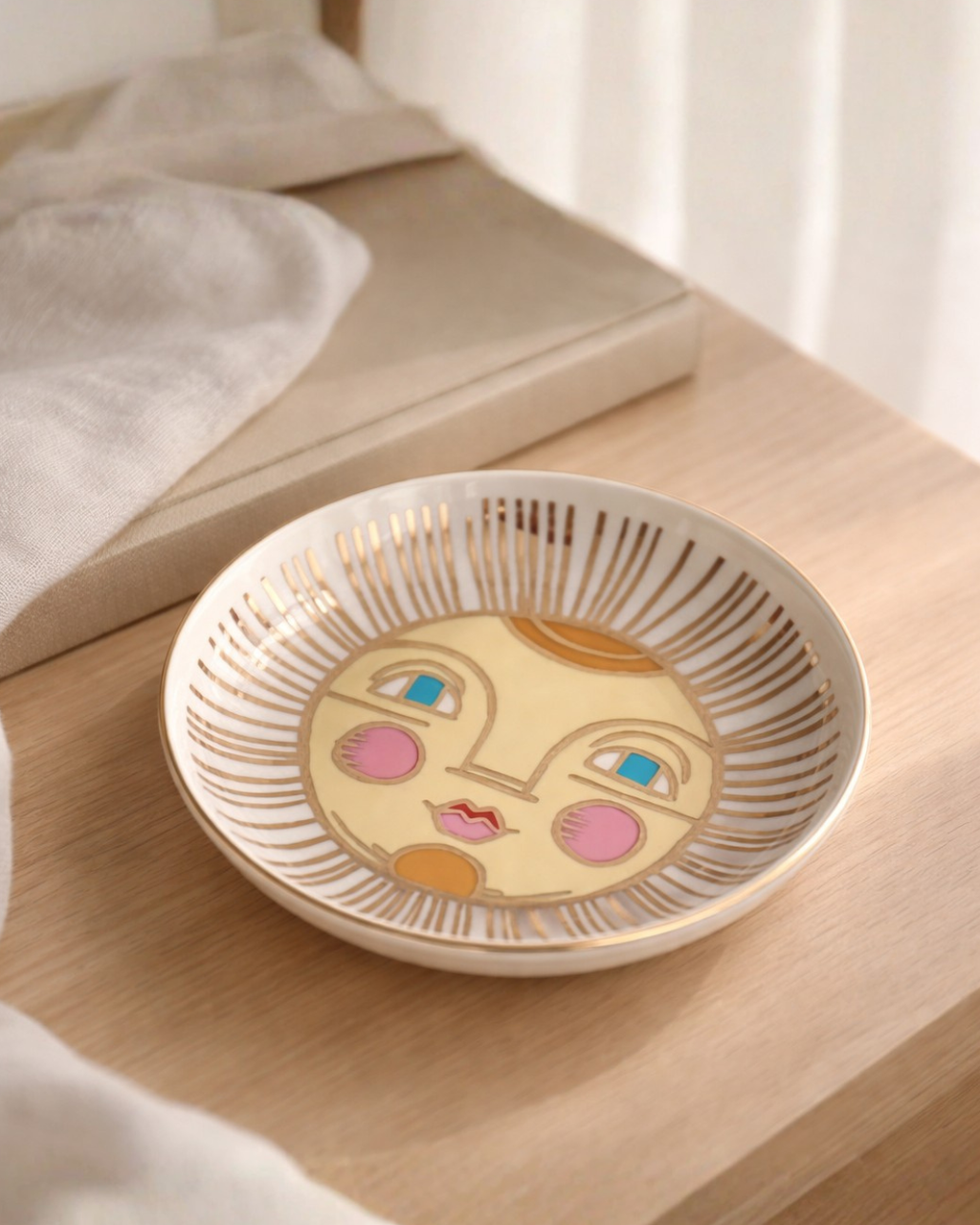 Sun face jewelry dish on wooden bedside table next to book and linen fabric, decorative ring holder dish for nightstand decor